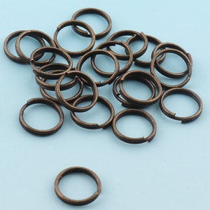 Könnte beinhalten: Ein Haufen von 18 antiken Bronze-Sprühringen, jeder mit einem Durchmesser von etwa 1,2 cm. Die Ringe sind in einem zufälligen Muster auf einer hellblauen Oberfläche angeordnet.