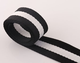 May include: Black and white striped webbing with a white stripe down the center. The webbing is rolled up and the white stripe is visible on the outside of the roll.