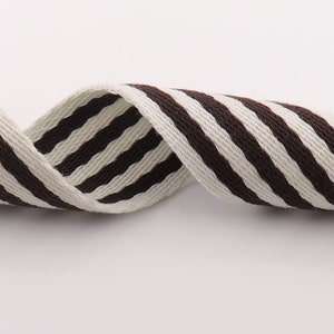 May include: Brown and white striped cotton webbing ribbon. The ribbon is woven with thick stripes and has a slightly textured surface.