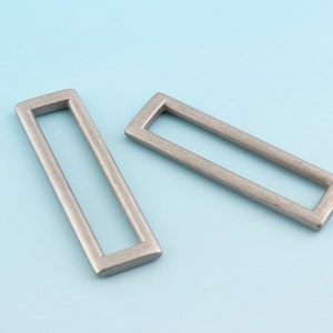 May include: Two silver metal rectangular frame buckles. The buckles are made of metal and have a smooth, polished finish.