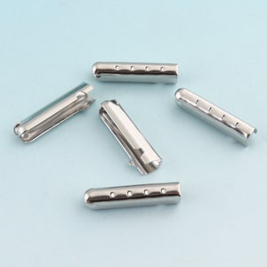 May include: Five silver metal eyelets, each with a cylindrical shape and a series of small holes along the length. The eyelets are arranged in a semi-circle on a light blue background.