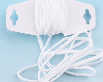 Op de afbeelding: Witte elastische koord gewikkeld om een witte plastic spoel met twee gaten. De koord ligt op een lichtblauwe achtergrond.