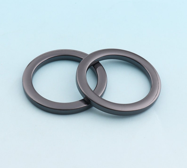 Puede incluir: Dos anillos de metal negro, uno ligeramente m&aacute;s grande que el otro, est&aacute;n entrelazados. Los anillos son lisos y tienen un acabado brillante.