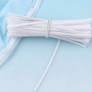 May include: A bundle of white plastic nose wire for face masks. The wire is bundled together with a rubber band.