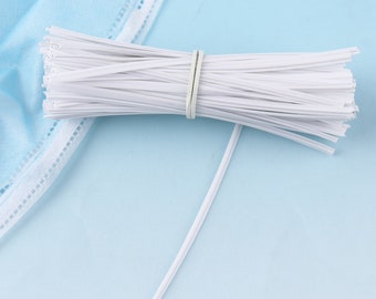 May include: A bundle of white plastic nose wire for face masks. The wire is bundled together with a rubber band.