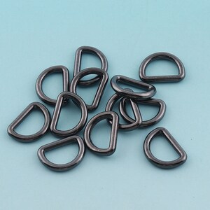 Puede incluir: Un grupo de 12 anillos en D de metal negro, también conocidos como anillos en D o anillos en forma de D. Estos anillos se utilizan comúnmente en la elaboración artesanal, la fabricación de joyas y el trabajo del cuero.