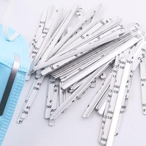 May include: A pile of silver metal nose wire strips for face masks. The strips are about 5 inches long and have adhesive backing. The strips are used to help the mask fit snugly over the nose.