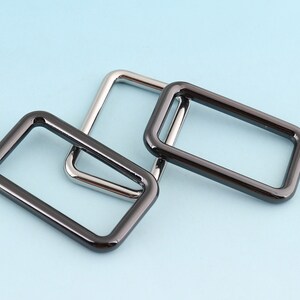 May include: Three metal rings, one silver and two black, are stacked on top of each other. The rings are all rectangular in shape and have rounded corners.
