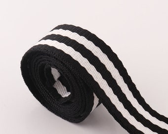 May include: Black and white striped webbing with a woven texture. The webbing is rolled up and the stripes are horizontal.