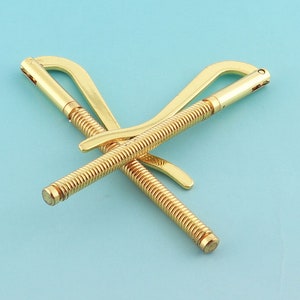 May include: A gold-colored metal money clip with a spring mechanism. The clip is designed to hold bills and cash securely.