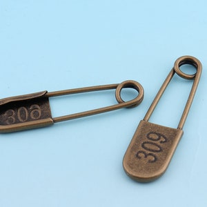 May include: Two antique gold safety pins with the numbers 306 and 309 engraved on them.