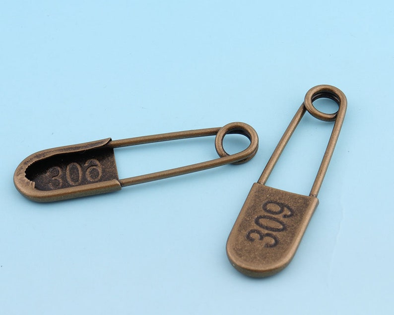 May include: Two antique gold safety pins with the numbers 306 and 309 engraved on them.