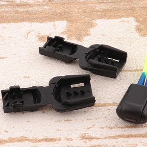 May include: Two black plastic cord locks with a yellow and blue cord. The cord locks have a series of teeth on one side and a hole on the other side.
