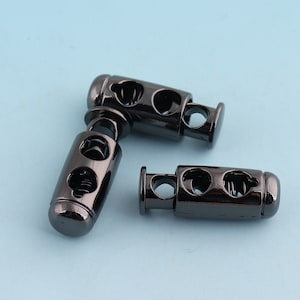 May include: Three black metal cord stoppers with a spring mechanism. The stoppers have two holes for threading cord through.
