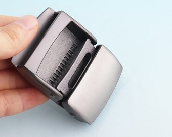 May include: A silver metal belt buckle with a smooth, flat surface and a textured, black, interlocking mechanism.