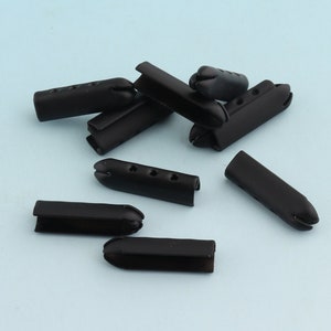 May include: A group of black plastic cord ends with four holes each. The cord ends are scattered on a light blue surface.