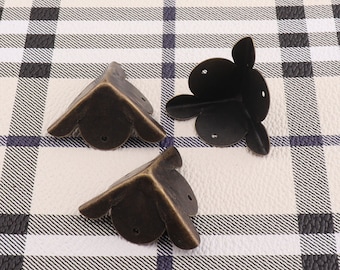 May include: Three antique brass corner protectors with a decorative scalloped edge. The protectors are designed to protect furniture corners from damage.