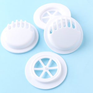 May include: Four white plastic face mask valve filters with different designs. The filters are round and have a small hole in the center.