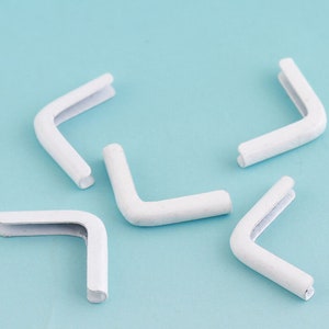 May include: Five white plastic corner protectors, each shaped like a right angle, are arranged on a light blue background.