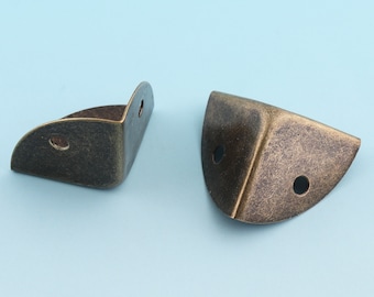 May include: Two antique gold corner brackets, each with a rounded edge and two holes. The brackets are made of metal and have a distressed finish.