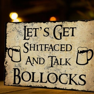 K&ouml;nnte beinhalten: Ein rustikales Holzschild mit dem Text "Let's Get Shitfaced and Talk Bollocks" in schwarzen Buchstaben. Zwei schwarze Silhouetten von Bierkr&uuml;gen befinden sich auf beiden Seiten des Textes.