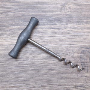 May include: A gray metal corkscrew with a T-shaped handle and a spiral worm. The handle has a textured surface. The corkscrew is designed for removing corks from wine bottles.