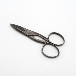 Può includere: Un paio di forbici vintage in metallo argentato con un piccolo manico. Le forbici hanno una punta appuntita e un piccolo foro nel manico.