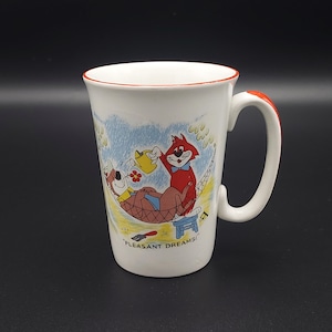 Peut inclure: Une tasse en céramique blanche avec une anse rouge. La tasse présente une illustration de dessin animé de deux chats dans un hamac avec le texte "Pleasant Dreams!" imprimé au bas.