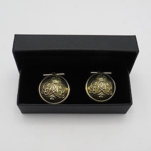 Peut inclure: Deux boutons de manchette dorés avec une couronne et des initiales ouvragées, présentés dans un coffret noir. Les boutons de manchette circulaires ont un design vintage. Le coffret est rectangulaire avec une finition mate. Chaque bouton mesure environ 2,5 cm de diamètre.