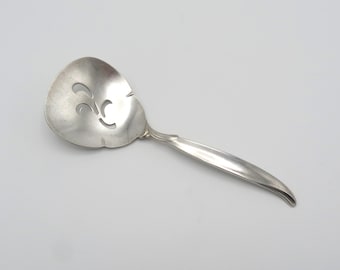 May include: A silver serving spoon with a decorative cut-out design in the bowl. The spoon has a long, curved handle.