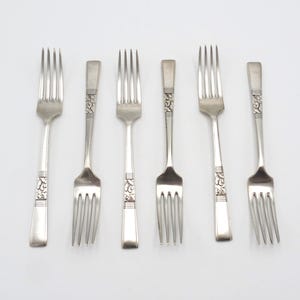 Peut inclure: Six fourchettes en argent avec des motifs ornés sur les manches. Les fourchettes sont disposées en rangée sur un fond blanc.
