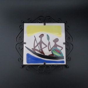 Peut inclure: Un carreau de céramique avec une image stylisée de deux personnages dans un bateau. Les personnages sont bruns, le bateau est noir et l'eau est bleue. L'arrière-plan est jaune. Le carreau est encadré d'un cadre en métal noir.