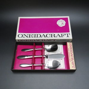 May include: A set of four OneidaCraft stainless steel spoons and a butter knife in a pink and white box. The box has the text "OneidaCraft" printed on it.