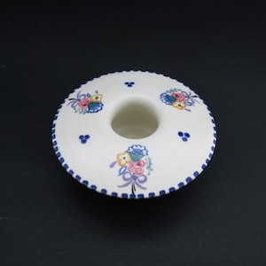 May include: White ceramic candle holder with a blue and white scalloped edge and floral designs in pink, yellow, blue, and green.