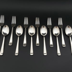 May include: A set of ten silver spoons and forks arranged in a row on a black background.