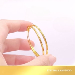 May include: A pair of gold hoop earrings with a textured finish. The earrings are held in a hand.