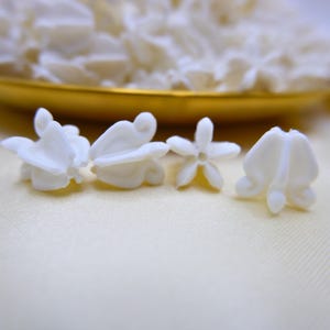 Comparison of small, medium, and large white faux crown flower beads displayed in a gold tray to show different sizes available.