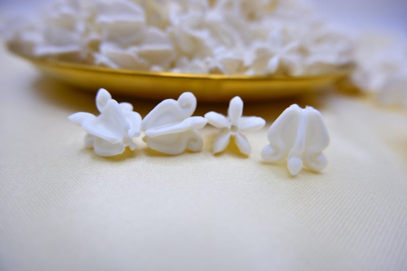 Comparison of small, medium, and large white faux crown flower beads displayed in a gold tray to show different sizes available.