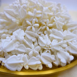 Detailed side view of premium white faux crown flower beads piled high, highlighting the petal shape and quality material.