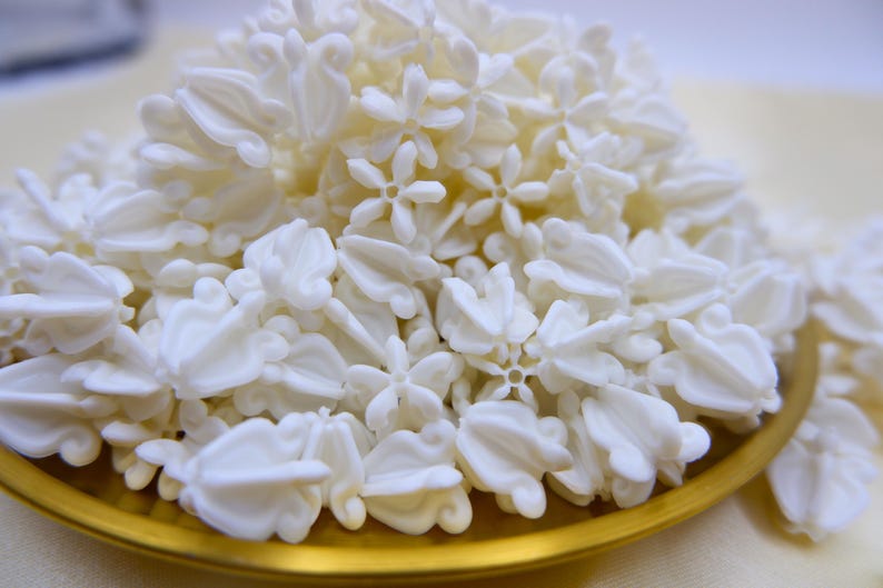 Detailed side view of premium white faux crown flower beads piled high, highlighting the petal shape and quality material.