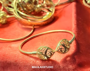 Könnte beinhalten: Ein goldfarbenes Armreif-Armband mit zwei durchbrochenen herzförmigen Anhängern. Das Armband liegt auf einem roten Stoffuntergrund.