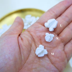 Hand showing three different sizes of white plastic crown flower beads to demonstrate the variety for Hawaiian lei and jewelry makers.