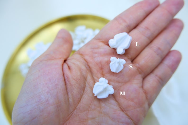 Hand showing three different sizes of white plastic crown flower beads to demonstrate the variety for Hawaiian lei and jewelry makers.
