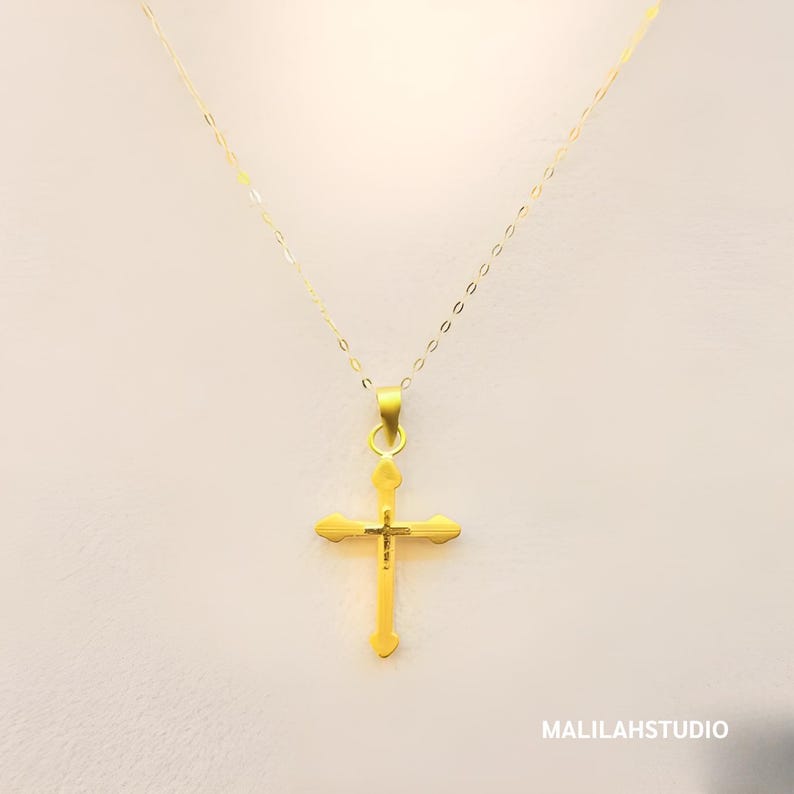 Primary product image of a 999 pure gold cross pendant displayed on a mannequin bust, hanging from a dainty gold-plated necklace chain. The pendant features a hollow design with smooth, heart-tipped arms and a polished yellow gold finish, offering a lightweight and elegant look. Ideal for spiritual gifting, Christian jewelry collections, or minimalist religious accessories. Branding "MALILAHSTUDIO" subtly appears in the corner, reinforcing premium handcrafted gold jewelry identity.
