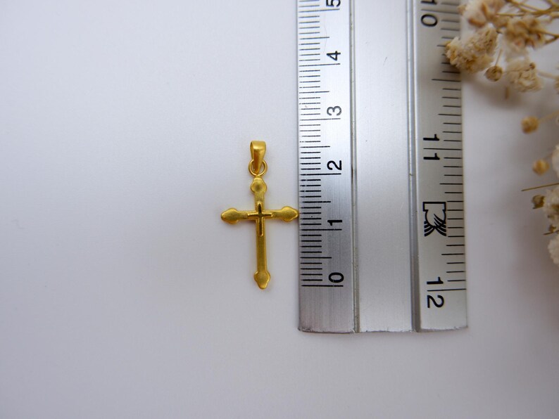 Close-up of a 999 pure gold cross pendant placed next to a silver measuring ruler, showing the pendant’s small and delicate size for accuracy. Ideal for customers seeking a lightweight gold Christian pendant for necklace chains. The minimalist hollow design makes it perfect for daily wear, baptism, or religious gifts. Includes dried white baby’s breath in the corner to enhance elegance. Great for Etsy searches related to gold religious jewelry and small gold cross charms.