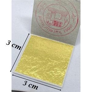 Könnte beinhalten: Ein quadratisches Blatt Goldblatt mit den Maßen 3 cm x 3 cm. Das Goldblatt befindet sich auf einem weißen Trägerpapier mit einem roten Stempel, auf dem in Thai "1000% Pure Gold Leaf" steht.