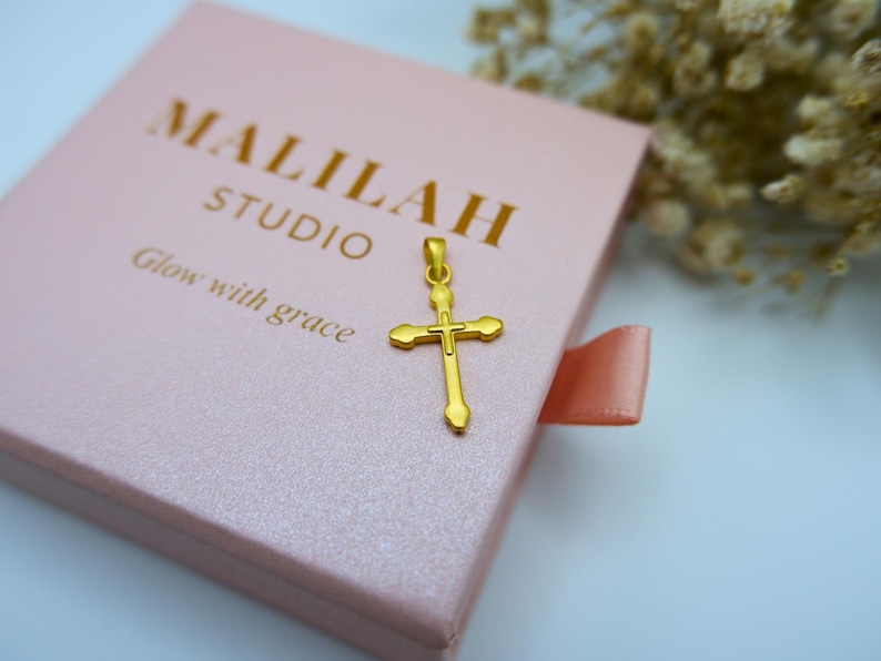 Elegant display of a 999 pure gold cross pendant resting on a soft pink jewelry box with "MALILAH STUDIO" and "Glow with grace" embossed in gold foil. This dainty, lightweight hollow cross charm is perfect as a religious gift, baptism necklace, or everyday Christian jewelry piece. Floral elements of dried white baby’s breath add a soft, feminine touch. Ideal for Etsy searches like gold cross pendant, real gold Christian charm, or minimalist gold faith jewelry.