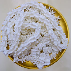 Overhead view of a completed white flower garland (Thai Malai) made from durable crown flower beads in a traditional gold tray.