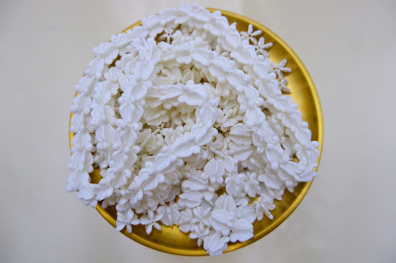 Overhead view of a completed white flower garland (Thai Malai) made from durable crown flower beads in a traditional gold tray.