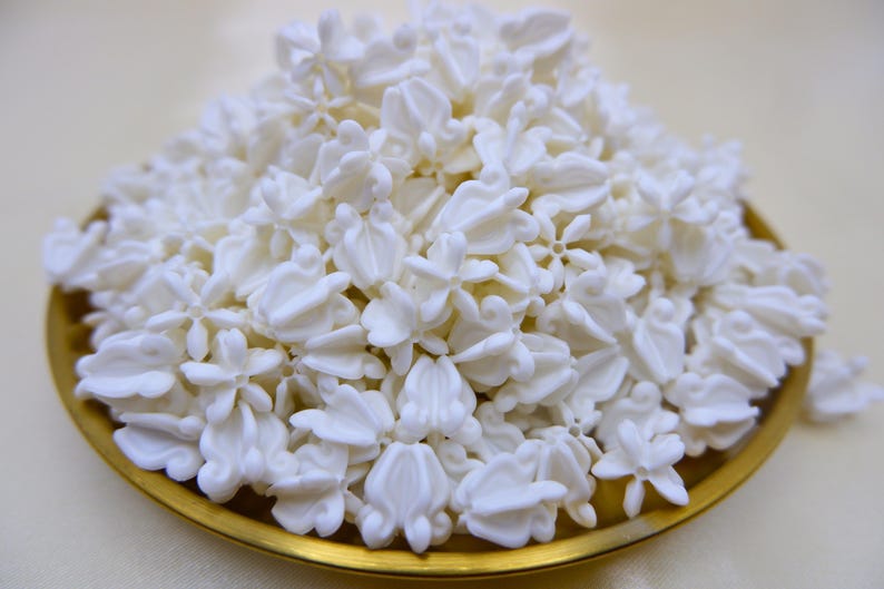 White faux crown flower beads (Thai Dok Rak) piled in a traditional Thai gold brass tray for Hawaiian lei making and graduation gifts.